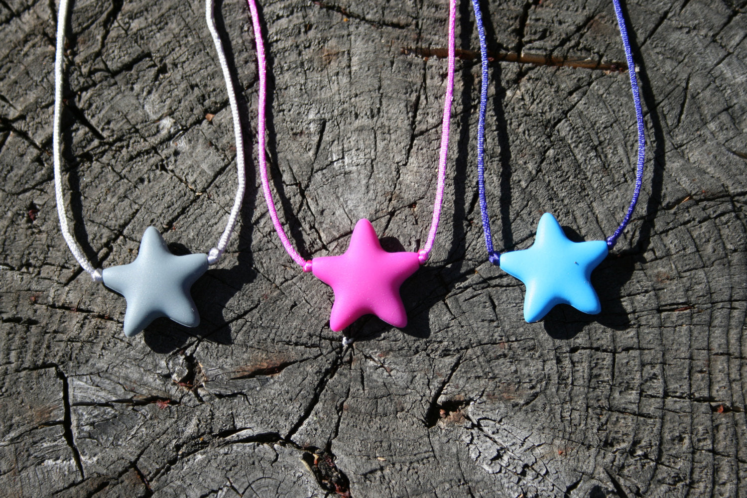 Sensory Necklace Chewable for Children with Star Pendant available in 3 colors: gray, hot pink, and aqua blue. Measures approximately 18", but can be made longer if needed. This pendant and is made from food-grade silicone, strung on a nylon cord, and finished off with a plastic clasp designed to pop open when pulled really hard. (Jewelry on wooden background)