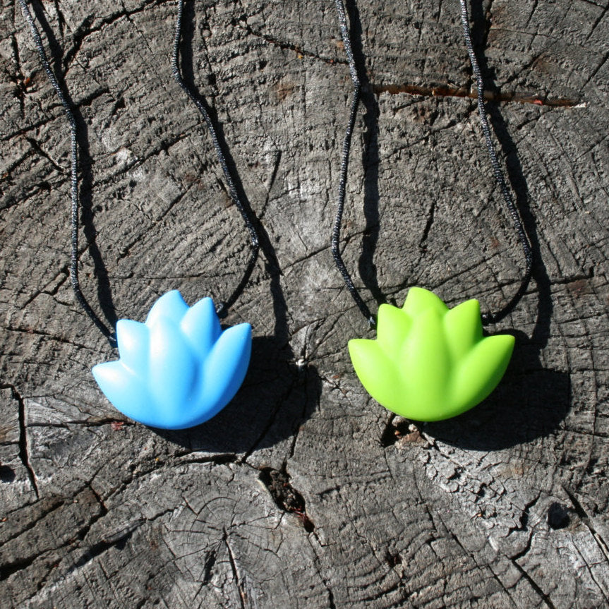 Sensory Necklace with Silicone Lotus Pendant - Available in 2 colors: Sky blue or Lime green -This pendant and is made from food-grade silicone, strung on a nylon cord, and finished off with a plastic clasp designed to pop open when pulled (Jewelry on wooden background)