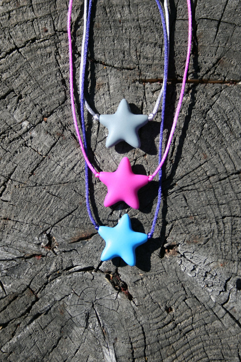 Sensory Necklace Chewable for Children with Star Pendant available in 3 colors: gray, hot pink, and aqua blue. Measures approximately 18", but can be made longer if needed. This pendant and is made from food-grade silicone, strung on a nylon cord, and finished off with a plastic clasp designed to pop open when pulled really hard. (Jewelry on wooden background)