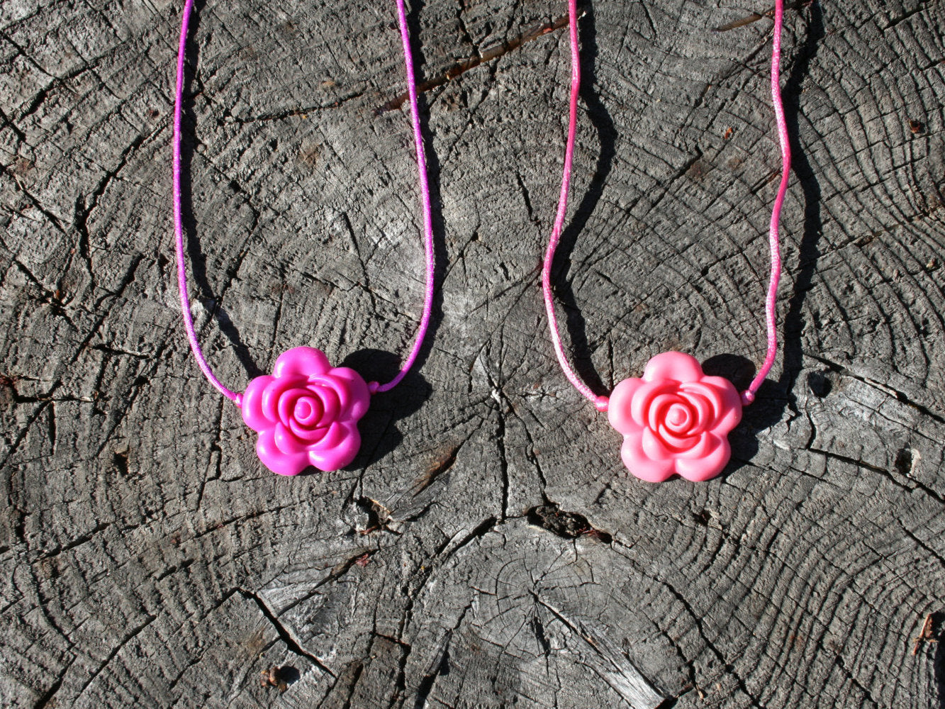 Sensory Necklace with Silicone Rose Pendant- Available in 2 colors: Hot Pink or Light Pink -This pendant and is made from food-grade silicone, strung on a nylon cord, and finished off with a plastic clasp designed to pop open when pulled (Jewelry on wooden background)