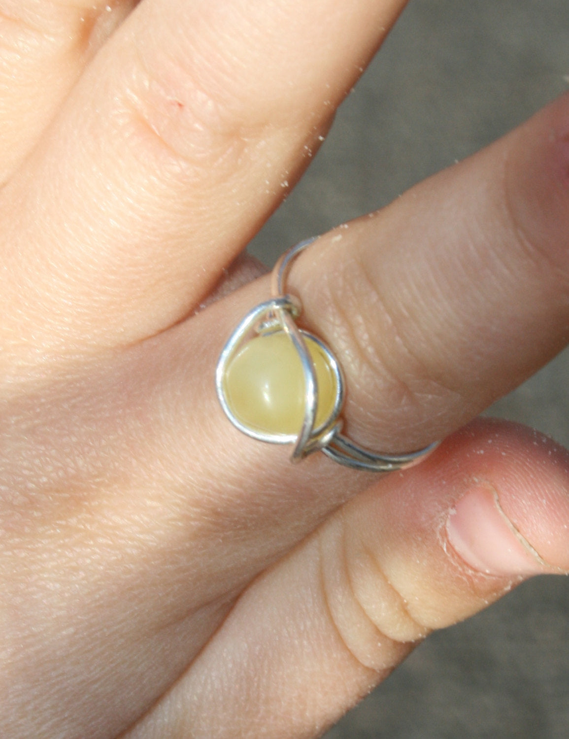 Picture of Baltic Amber Ring, Sterling Silver, Wire Wrapped, Unpolished, Raw, Any Size. This can be made with any color of amber: Milky(pictured), Lemon, Honey, Cognac, Coffee, or Green. The amber bead sits against the finger and allows the amber to work its magic! (Ring on model finger)