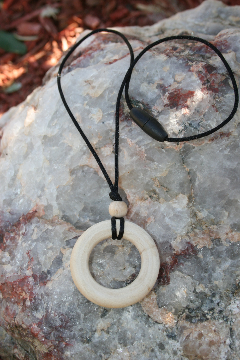 Sensory Necklace Wooden - for Children to Wear and Chew on - Child Sized Nursing Necklace -this 1 3/4" pendant and bead is made from solid Maple hardwoods sourced directly from Oregon, USA! It is strung on a nylon cord and finished off with a plastic clasp designed to pop open when pulled (Jewelry on rock background)