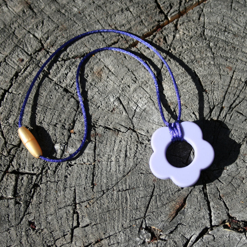 Picture ofSensory Necklace for Children with Chewable Flower Pendant - This pendant can withhold the mouth of a heavy chewer! Available in 2 colors: lavender and pink! This pendant and is made from food-grade silicone, strung on a nylon cord, and finished off with a plastic clasp. (Jewelry on wooden background)  