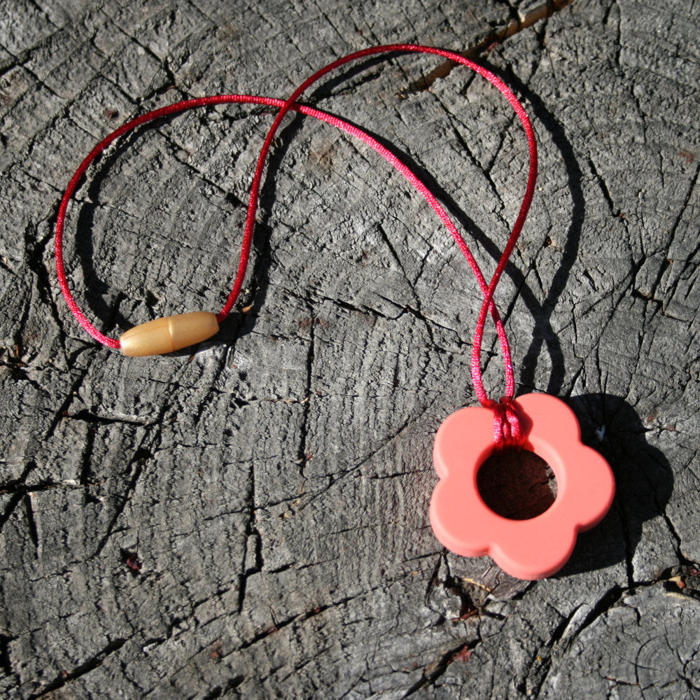 Picture ofSensory Necklace for Children with Chewable Flower Pendant - This pendant can withhold the mouth of a heavy chewer! Available in 2 colors: lavender and pink! This pendant and is made from food-grade silicone, strung on a nylon cord, and finished off with a plastic clasp. (Jewelry on wooden background)  