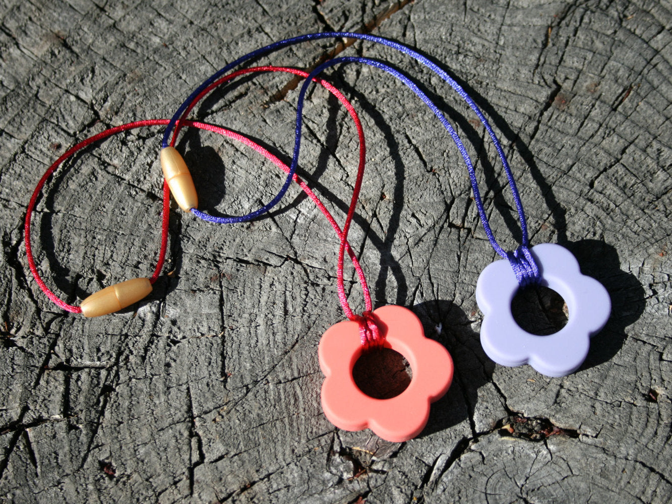 Picture ofSensory Necklace for Children with Chewable Flower Pendant - This pendant can withhold the mouth of a heavy chewer!   Available in 2 colors: lavender and pink!  This pendant and is made from food-grade silicone, strung on a nylon cord, and finished off with a plastic clasp. (Jewelry on wooden background)