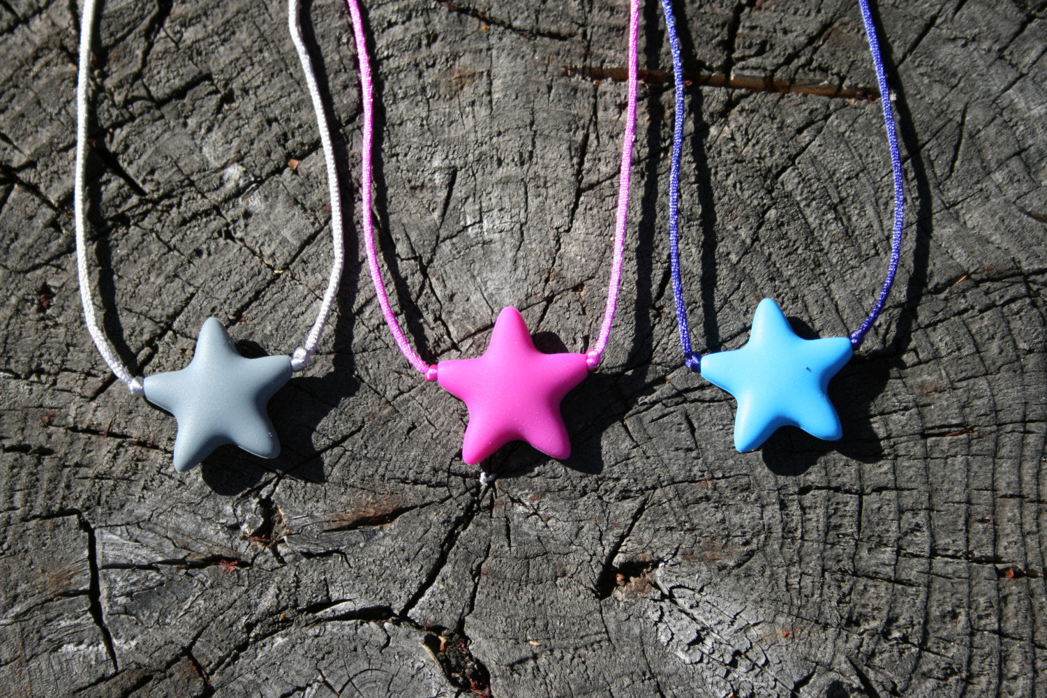 Sensory Necklace Chewable for Children with Star Pendant available in 3 colors: gray, hot pink, and aqua blue. Measures approximately 18", but can be made longer if needed. This pendant and is made from food-grade silicone, strung on a nylon cord, and finished off with a plastic clasp designed to pop open when pulled really hard. (Jewelry on wooden background)  