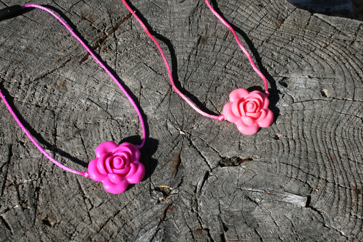 Sensory Necklace with Silicone Rose Pendant- Available in 2 colors: Hot Pink or Light Pink -This pendant and is made from food-grade silicone, strung on a nylon cord, and finished off with a plastic clasp designed to pop open when pulled (Jewelry on wooden background)  