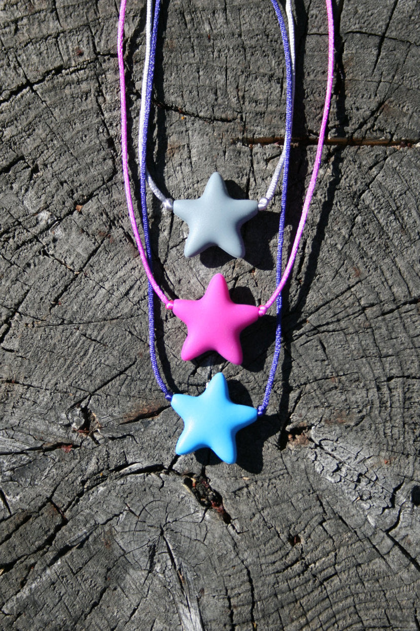 Sensory Necklace Chewable for Children with Star Pendant available in 3 colors: gray, hot pink, and aqua blue. Measures approximately 18", but can be made longer if needed. This pendant and is made from food-grade silicone, strung on a nylon cord, and finished off with a plastic clasp designed to pop open when pulled really hard. (Jewelry on wooden background)  