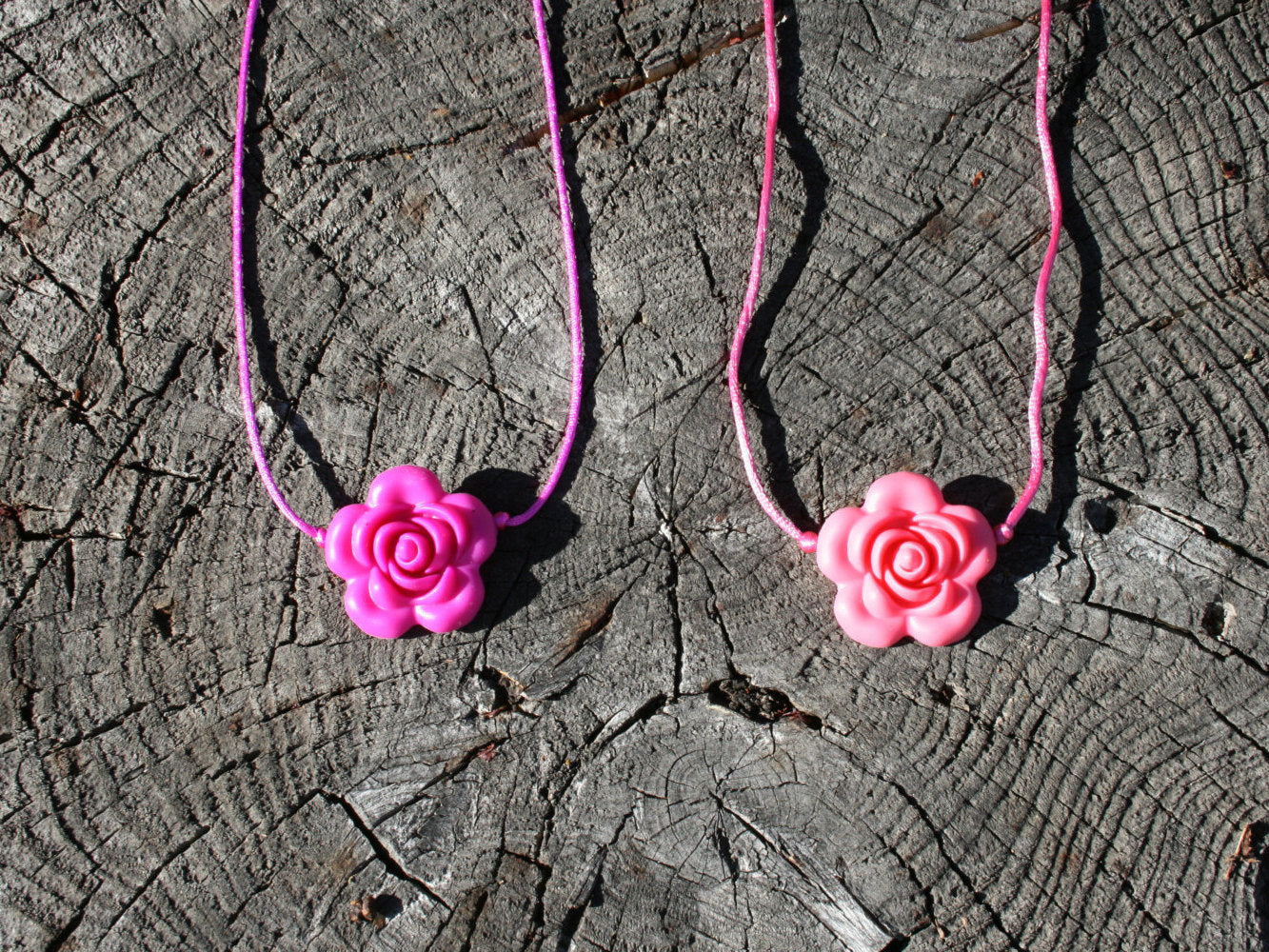 Sensory Necklace with Silicone Rose Pendant- Available in 2 colors: Hot Pink or Light Pink -This pendant and is made from food-grade silicone, strung on a nylon cord, and finished off with a plastic clasp designed to pop open when pulled (Jewelry on wooden background)  