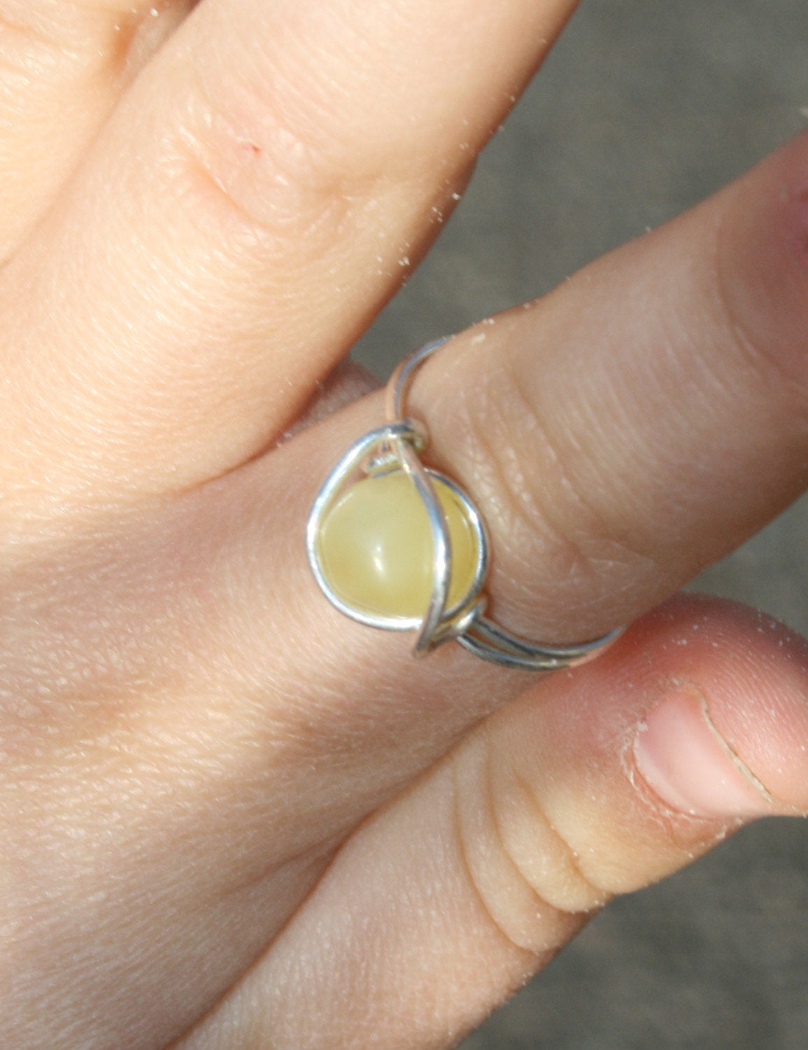 Picture of Baltic Amber Ring, Sterling Silver, Wire Wrapped, Unpolished, Raw, Any Size. This can be made with any color of amber: Milky(pictured), Lemon, Honey, Cognac, Coffee, or Green. The amber bead sits against the finger and allows the amber to work its magic! (Ring on model finger) 