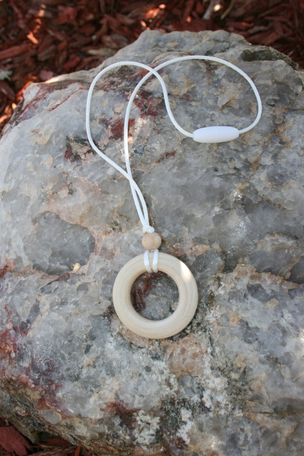 Sensory Necklace Wooden - for Children to Wear and Chew on - Child Sized Nursing Necklace -this 1 3/4" pendant and bead is made from solid Maple hardwoods sourced directly from Oregon, USA! It is strung on a nylon cord and finished off with a plastic clasp designed to pop open when pulled (Jewelry on rock background)  